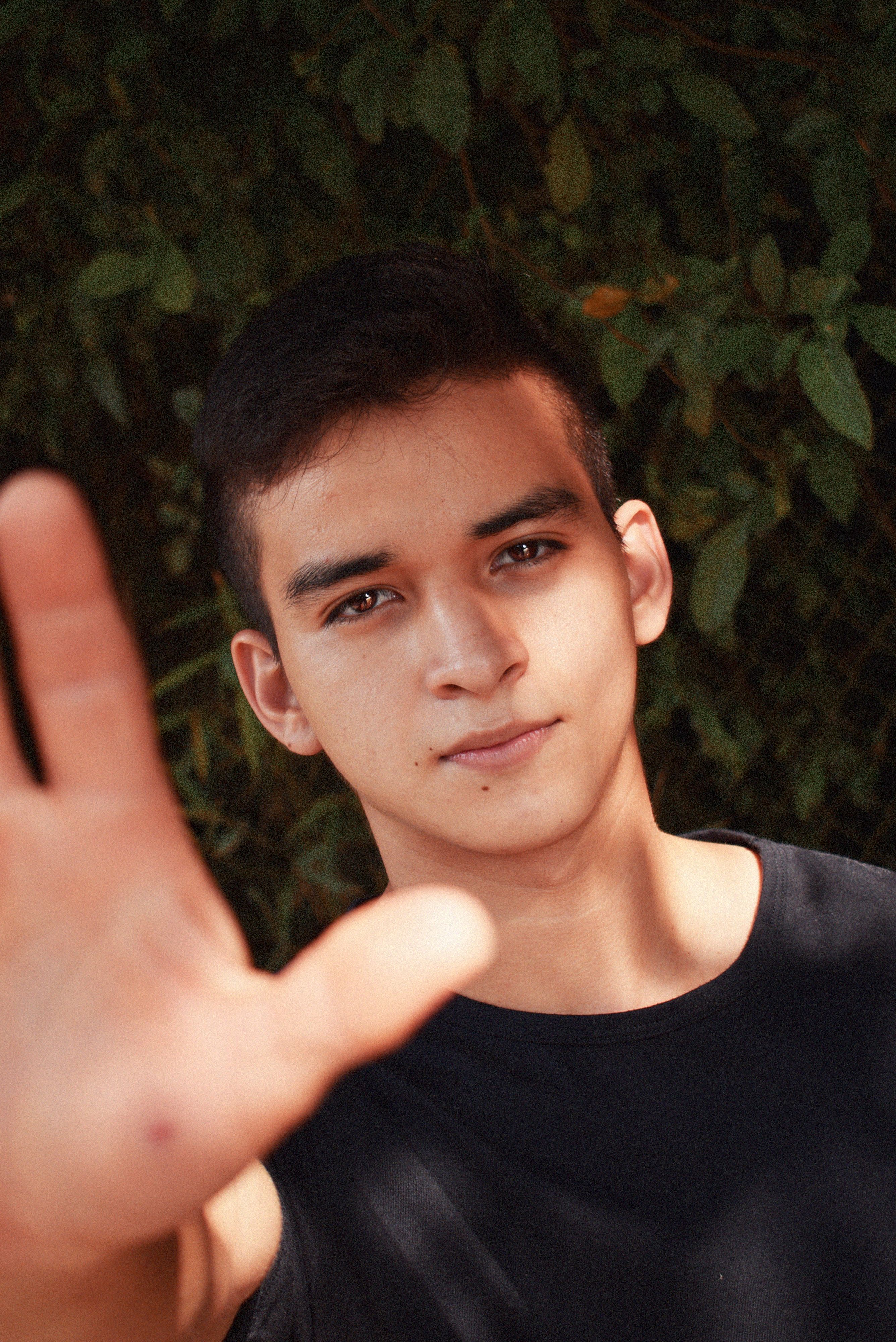 Portrait of a young man outdoors, reaching towards the camera with a serious expression.