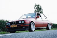 一辆老式红色汽车停在乡村路边，展示着经典的设计