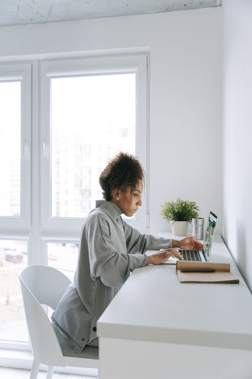 Free A woman working on her laptop at a home office desk in a modern, bright room. Stock Photo