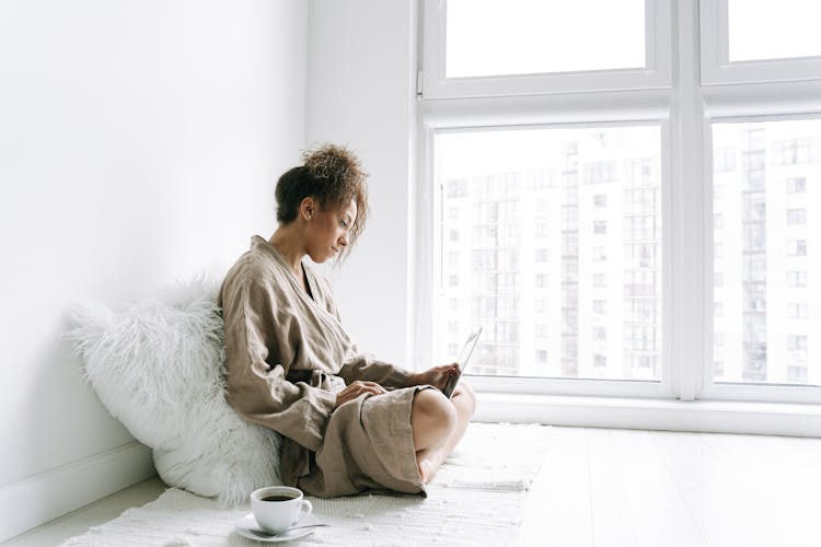 A Woman In Brown Robe Sitting On The Floor While Using Her Laptop