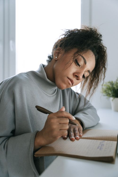Free African American woman with afro hair writing in a notebook indoors. Stock Photo