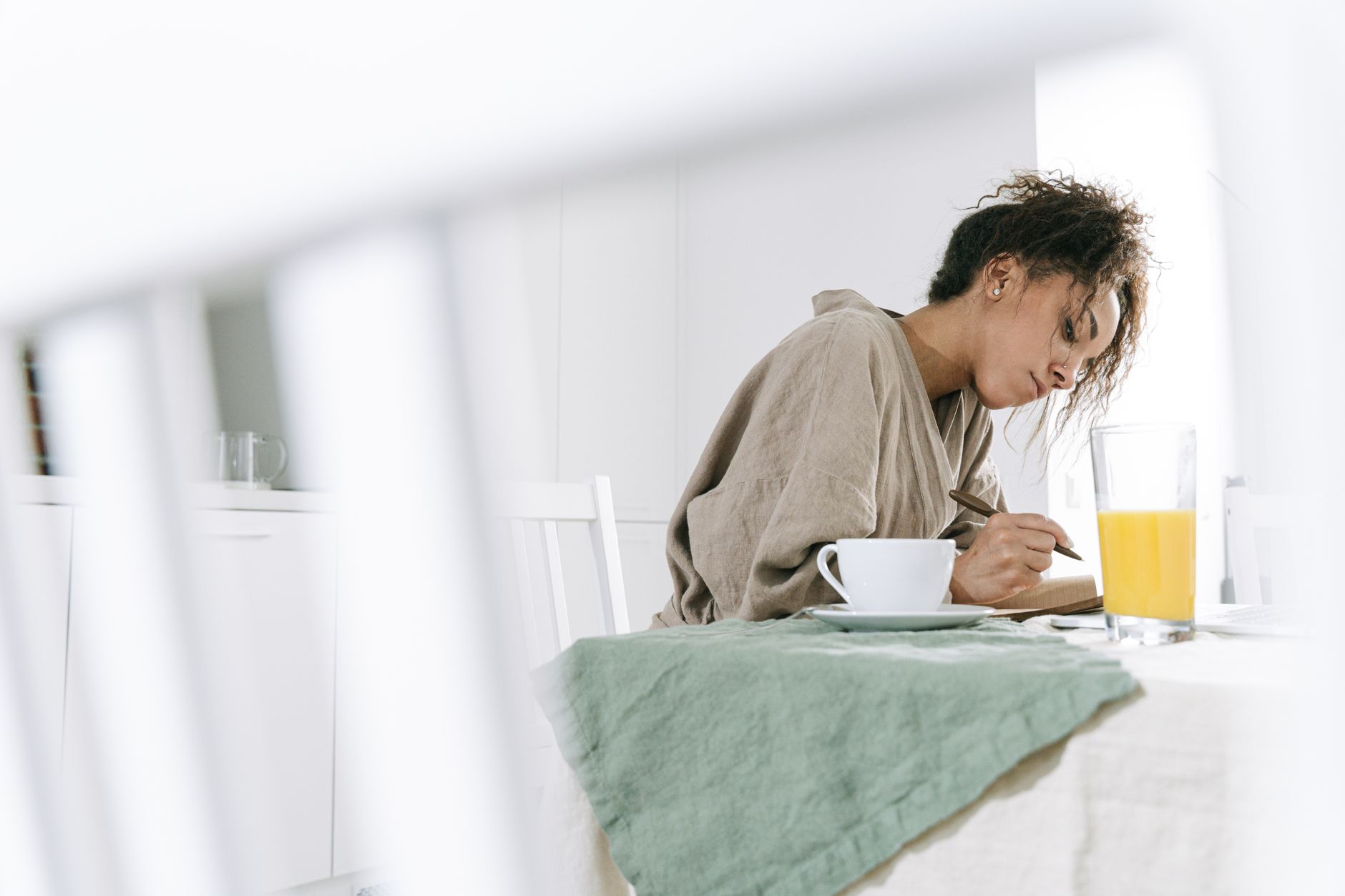 A woman writing in a notebook at a kitchen table in morning light