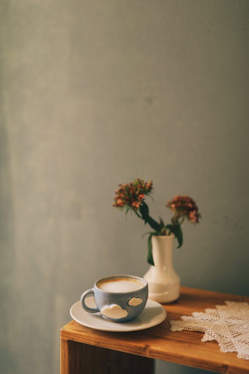 Free Cup of cappuccino placed on table with flowers in vase Stock Photo