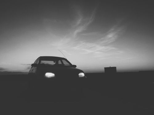 Free Black and white photo of a car silhouette on a road at dusk with a dramatic sky. Stock Photo