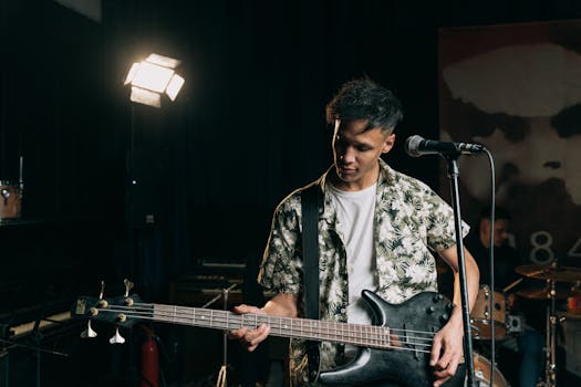 A young adult playing bass guitar during a live performance indoors, captured in a moody setting.