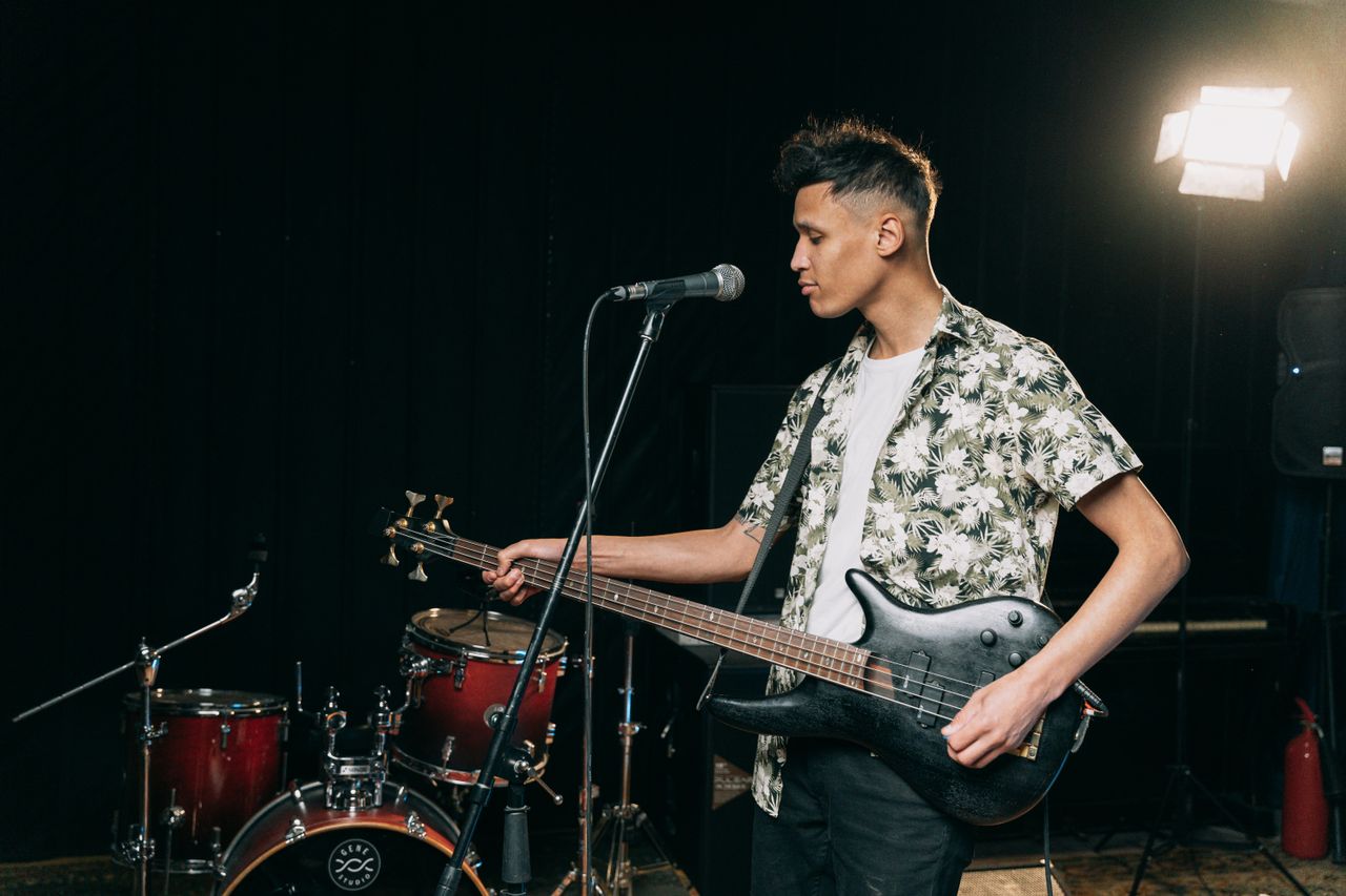 a male musician in a floral shirt playing a bass guitar on stage durin
