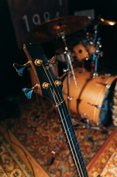 Detailed close-up of a bass guitar headstock with a drum set in a studio setting.