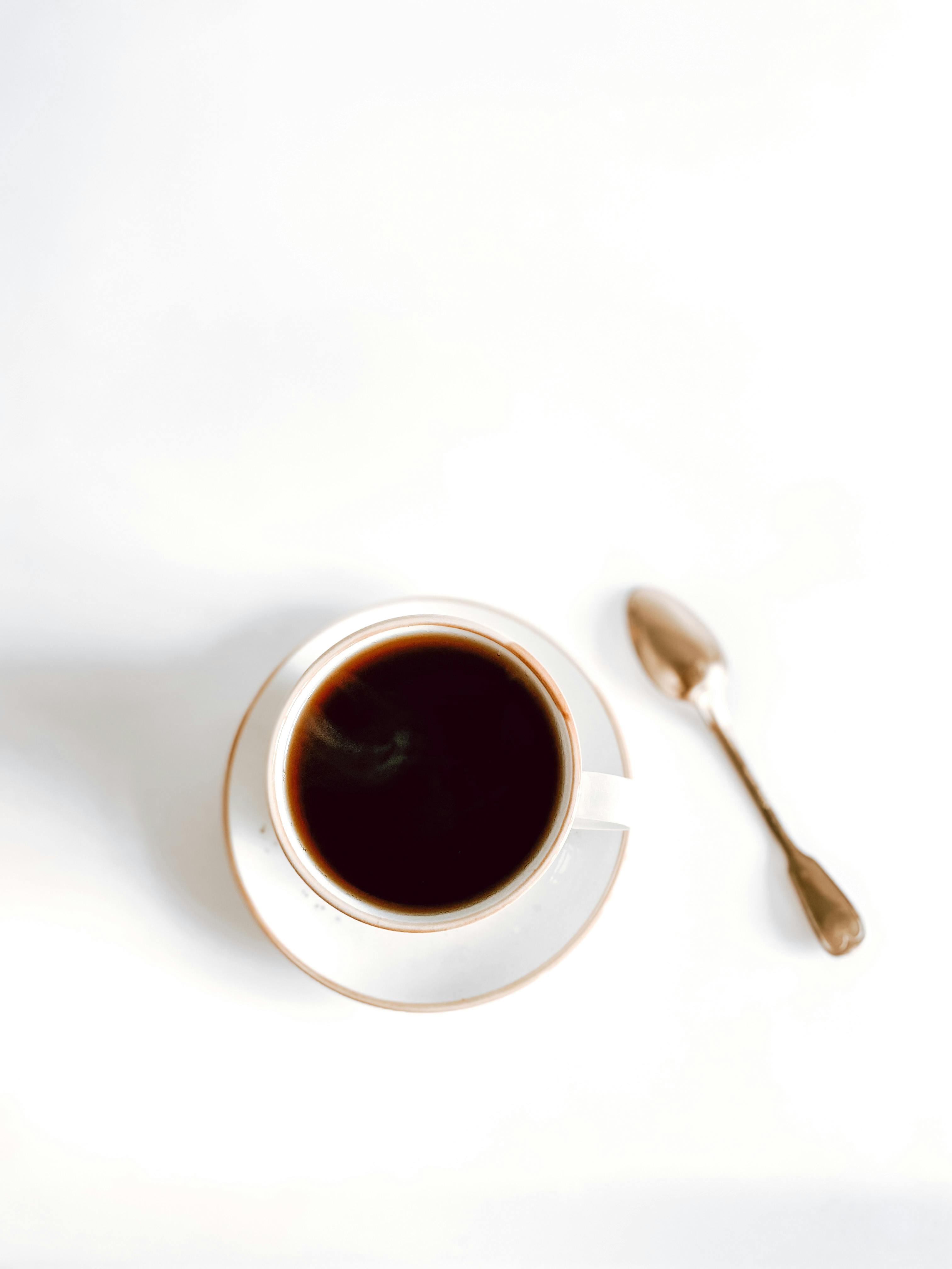 Elegant overhead shot of a coffee cup and spoon on a white background, emphasizing simplicity.