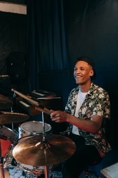 A joyful drummer with a floral shirt plays drums in an indoor studio environment.