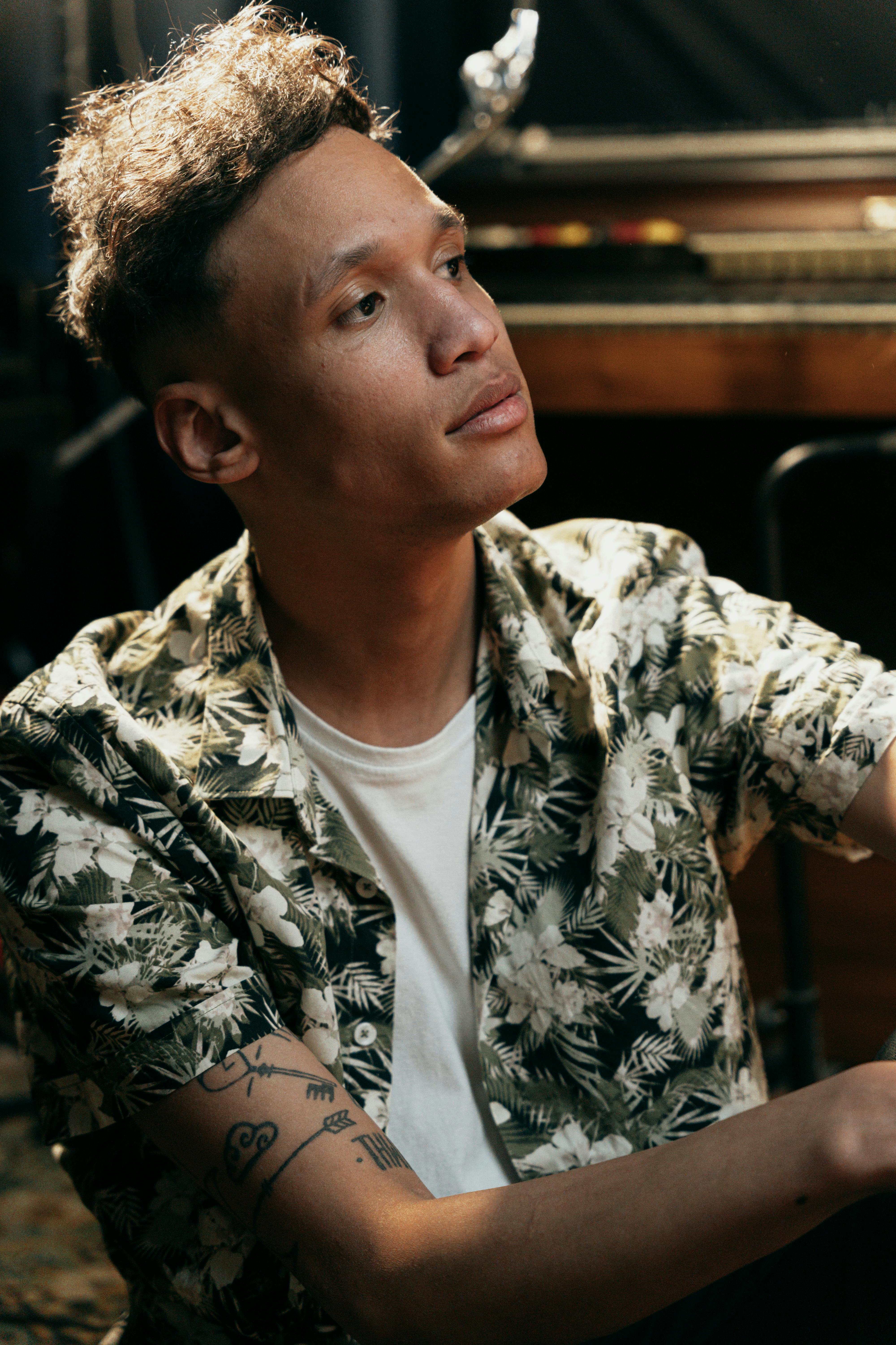Side view portrait of a young man in a floral shirt indoors, looking reflective in soft lighting.