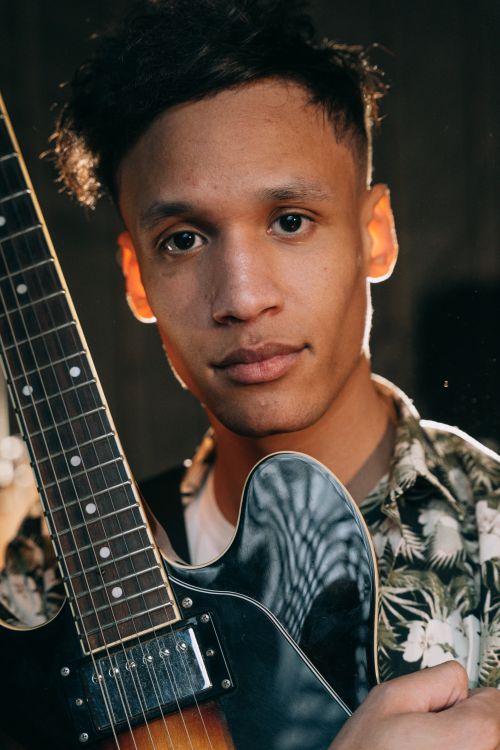 Free A man in a floral shirt holds a guitar against a dark background. Stock Photo