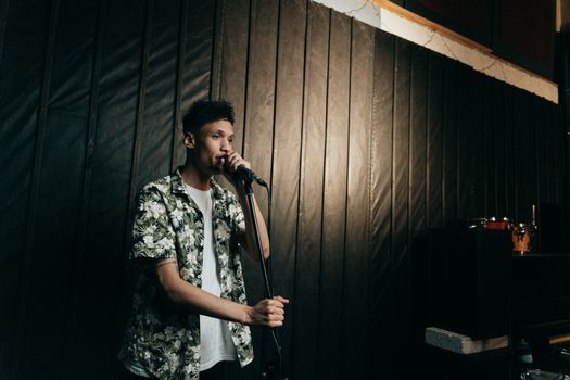 A young man sings passionately into a microphone on stage, wearing a floral shirt.