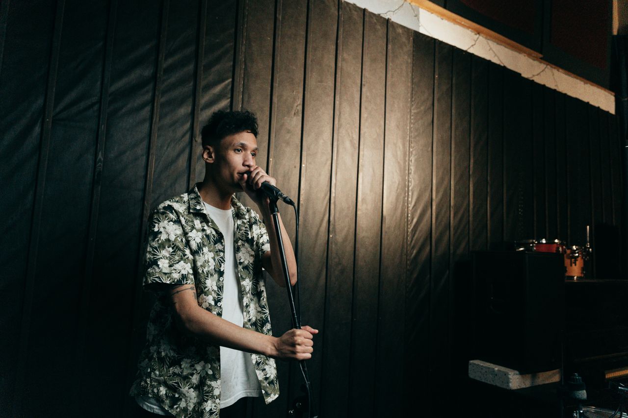 a young man sings passionately into a microphone on stage wearing a fl