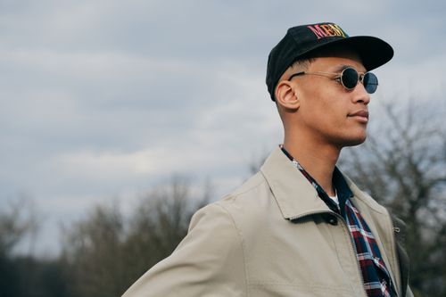 Free Portrait of a stylish man with sunglasses and cap, standing outdoors in a relaxed pose. Stock Photo