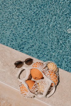 A relaxing summer setup with oranges and sunglasses by the pool, perfect for vacation and leisure.
