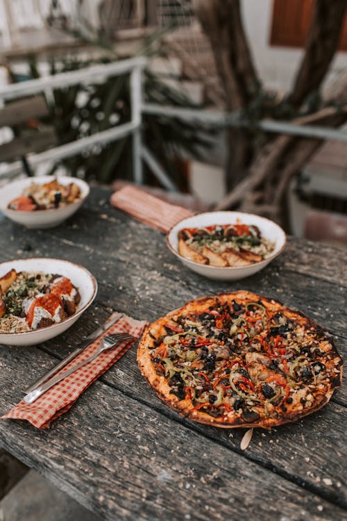 Plate Of Pizza And Dish Bowls With Food On Wooden Table
