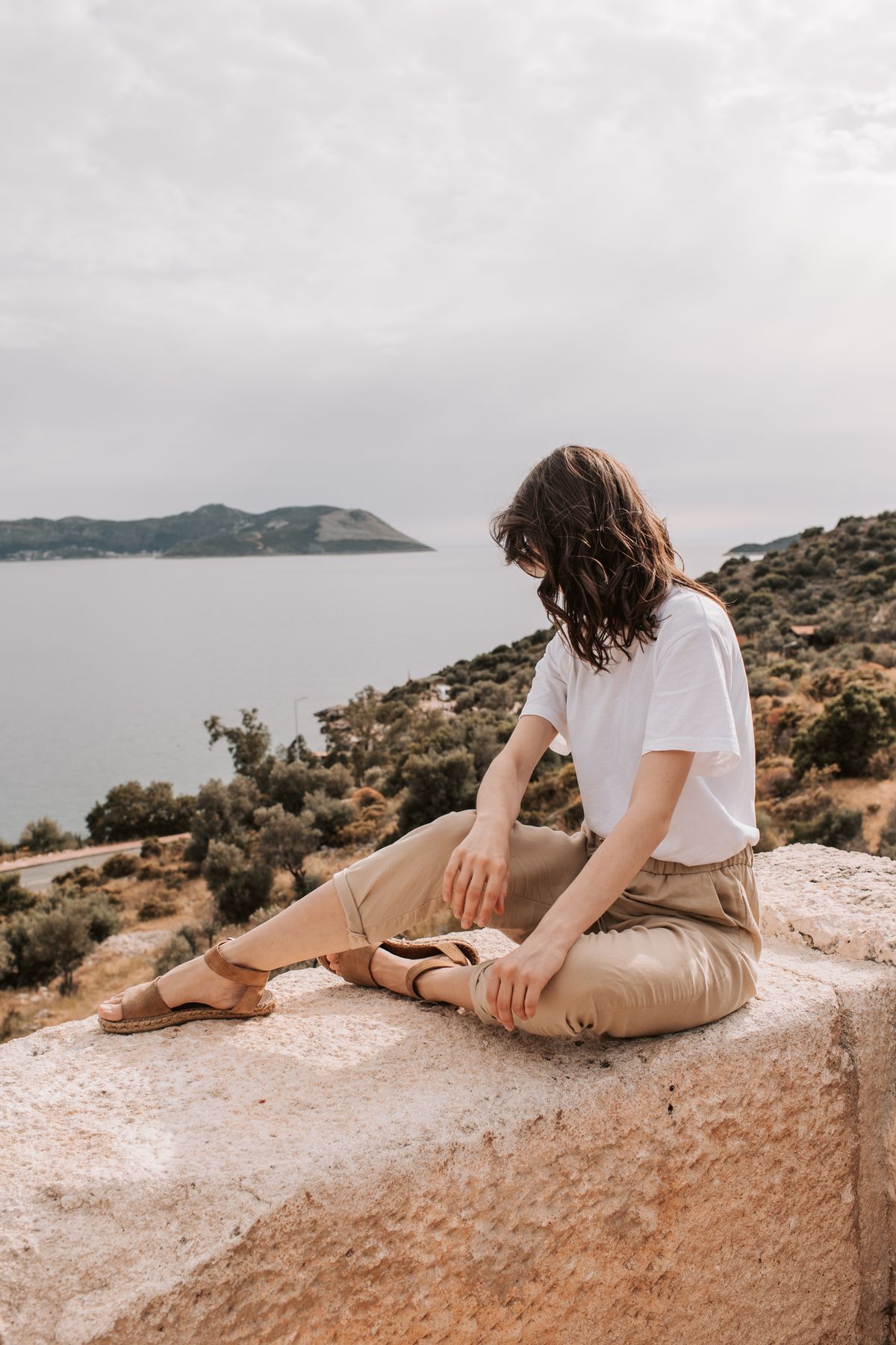 A woman sitting on a concrete wall facing the Mediterranean sea — the Riviera mood of the capri pant