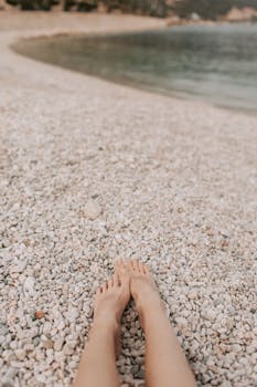 Feet resting on a gravel beach by the sea, perfect for summer relaxation and travel vibes.