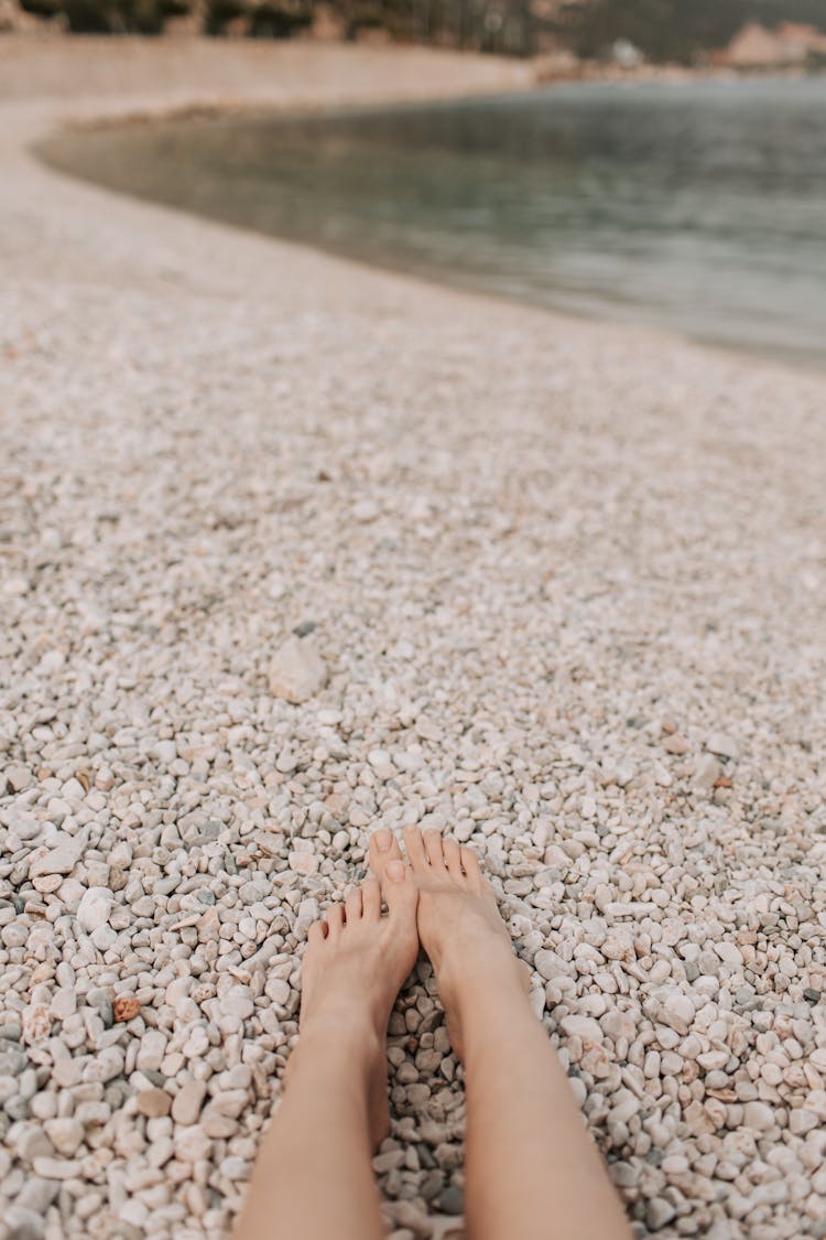 Persons Feet On White And Brown Stones Near Body Of Water