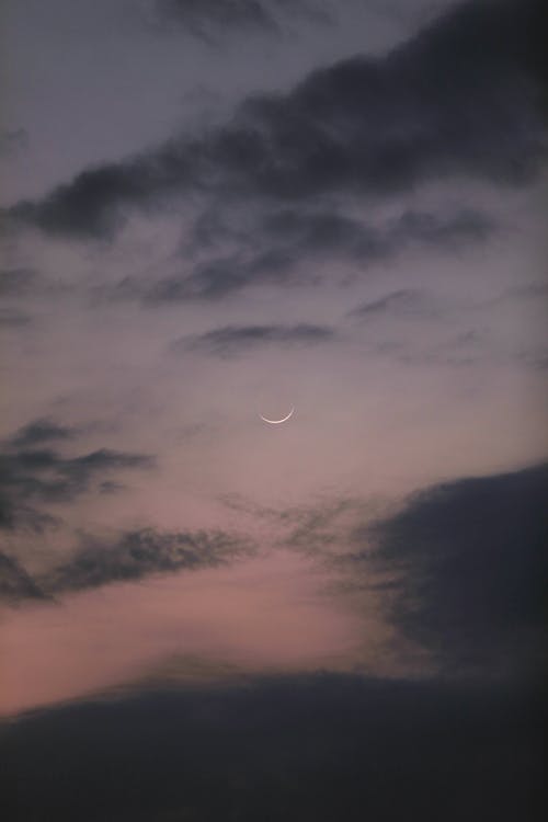 Free Thin crescent moon shining high in air on sky with dark clouds at sunset time in nature on summer evening Stock Photo