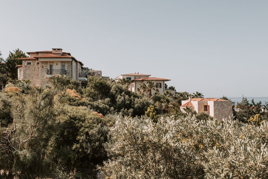 Mediterranean stone villas with terracotta roofs on a vegetated coastal hillside overlooking the sea