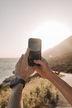Person photographing a beautiful coastal sunset with a smartphone, capturing vacation memories.