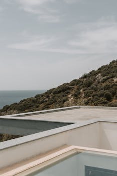 A modern rooftop terrace overlooking a lush hillside and the ocean under a clear sky.