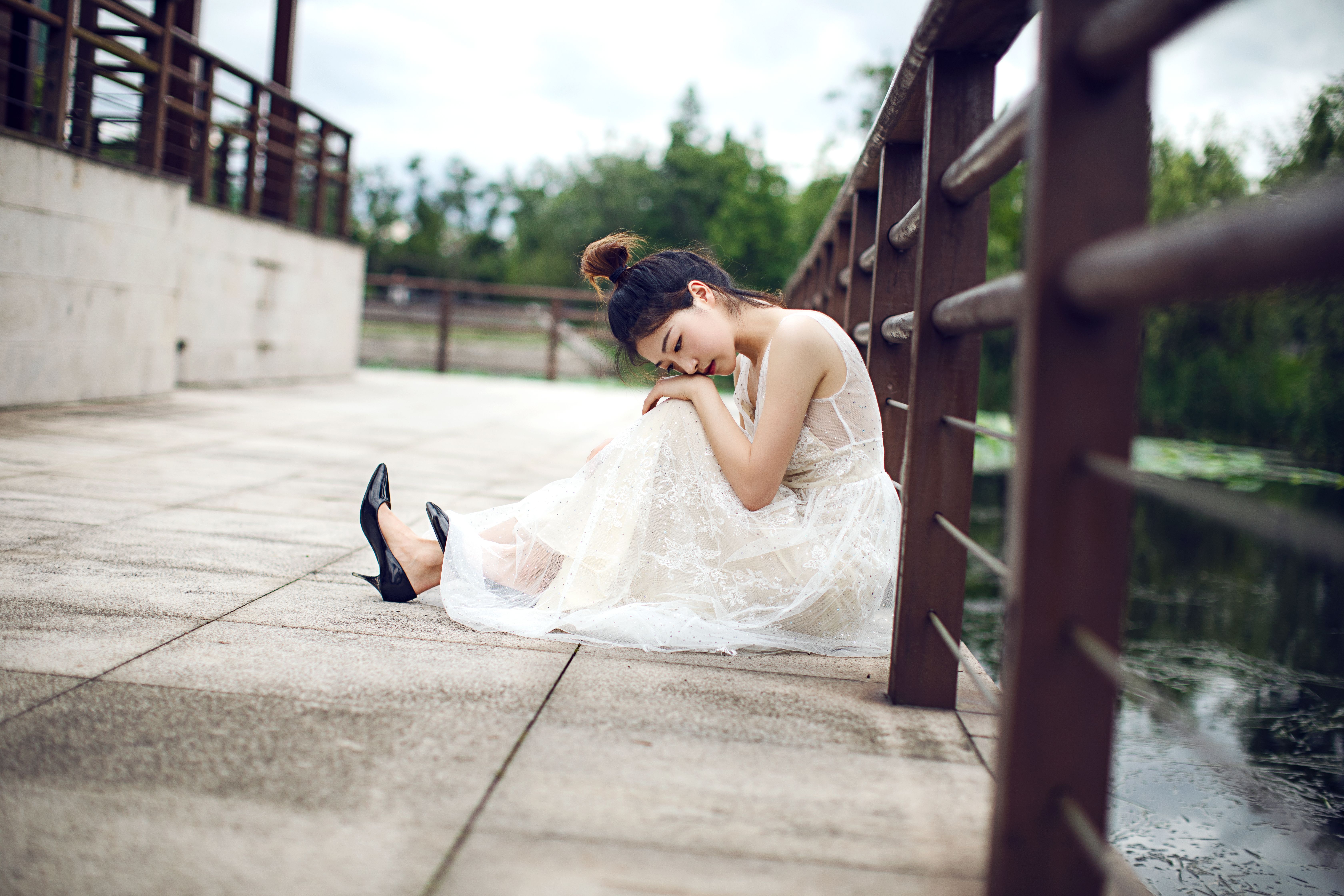 A serene bride in an elegant dress rests on a bridge, exuding calmness and beauty.