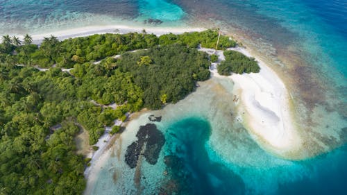 Spectacular drone shot of tropical island with lush vegetation and white sandy beach washed by peaceful azure ocean waters