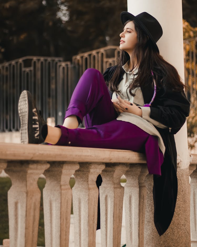 Female Fashion Model Sitting On Top Of An Outdoor Balustrade