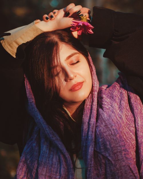 Free A serene woman with eyes closed holds a flower outdoors, basking in the warm sunlight. Stock Photo