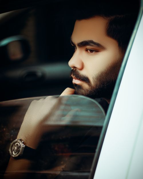 Free A thoughtful young man with a beard and watch gazes out a car window, creating a reflective mood. Stock Photo