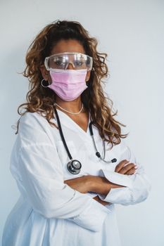 Female doctor with eyeglasses and face mask standing confidently with arms crossed.
