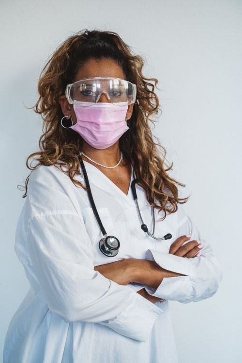 Free Female doctor with eyeglasses and face mask standing confidently with arms crossed. Stock Photo