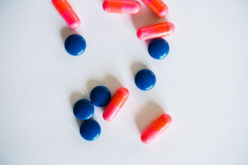A collection of pink capsules and blue pills scattered on a white background.