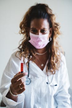 Doctor wearing mask holding a red syringe, focused, wearing a lab coat.