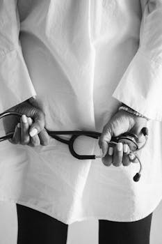 Black and white image of a doctor holding a stethoscope behind their back.