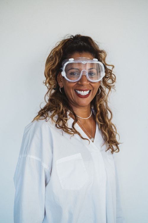 Free Confident woman in lab coat and goggles smiling at camera indoors. Stock Photo