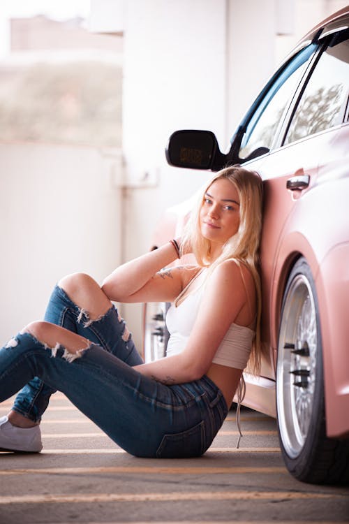 Free A Woman in Denim Jeans Sitting on the Floor while Leaning on the Car Stock Photo