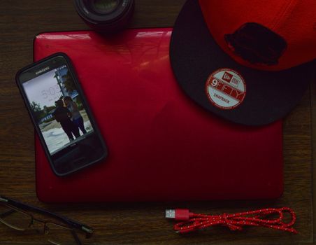 Stylish workspace with red laptop, cap, lens, and smartphone on a wooden desk.