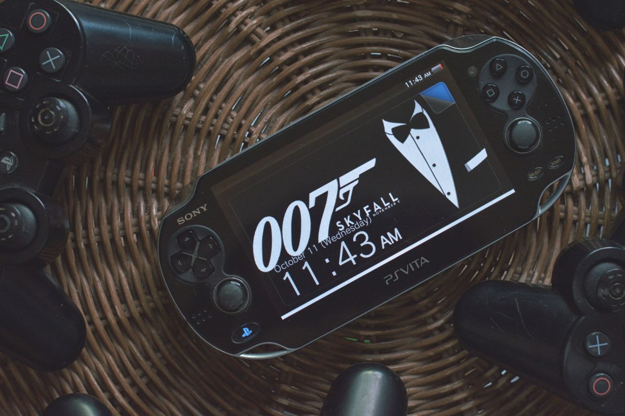 ps vita showing 007 theme surrounded by playstation controllers on a w