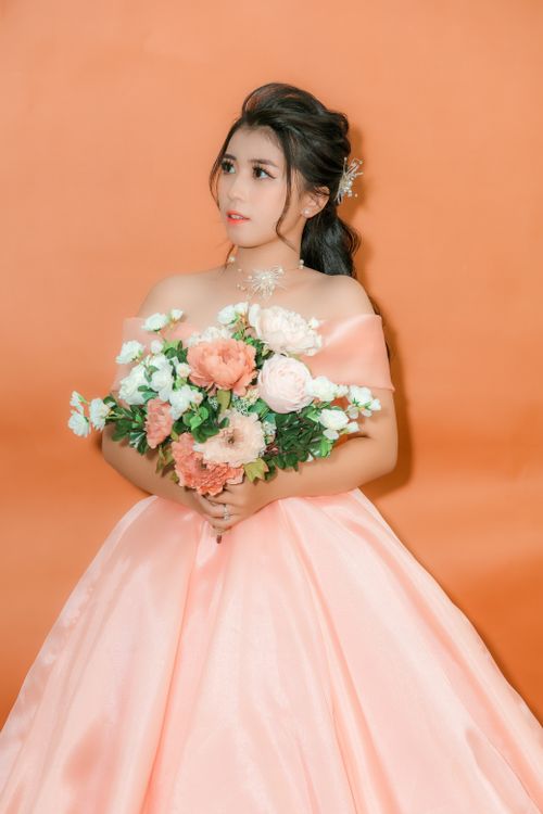 Free Elegant woman in a pink gown holding a colorful bouquet against an orange background. Stock Photo