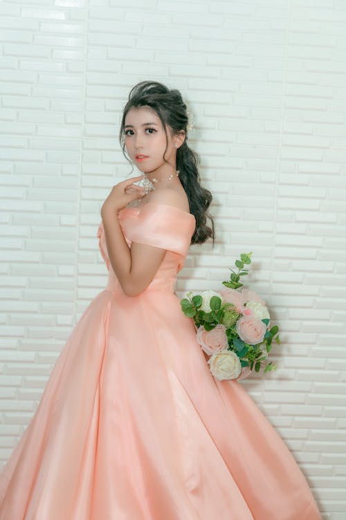 Woman in Peach Dress Standing Beside a Wall