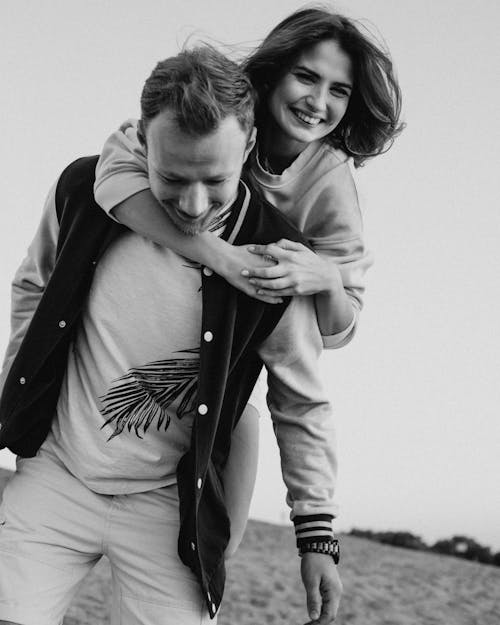 Free Black and white of positive young couple in trendy clothes hugging while smiling and standing in nature Stock Photo