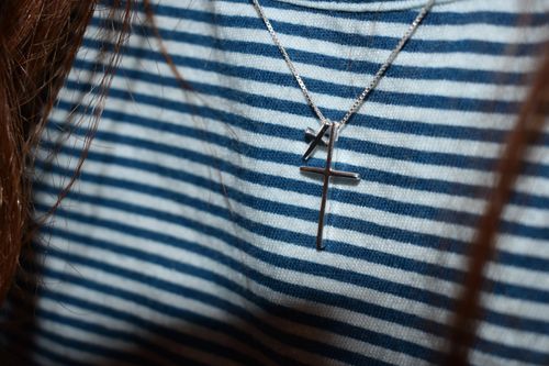 Free A silver cross necklace showcased on a blue and white striped shirt, highlighting minimalist fashion. Stock Photo
