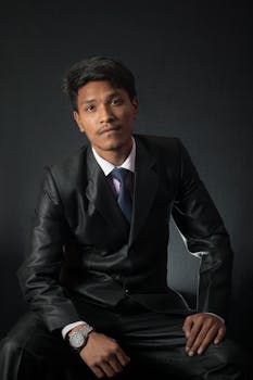 A confident young businessman posing in a black suit against a dark background.