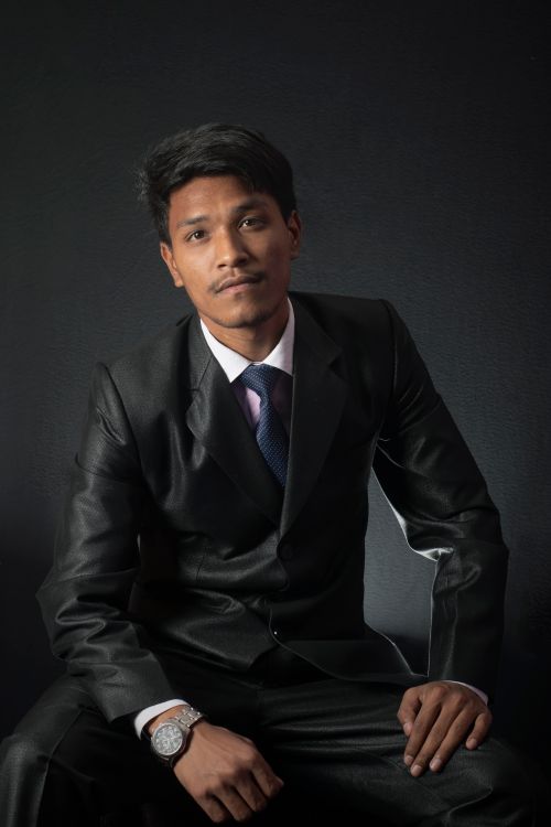 Free A confident young businessman posing in a black suit against a dark background. Stock Photo