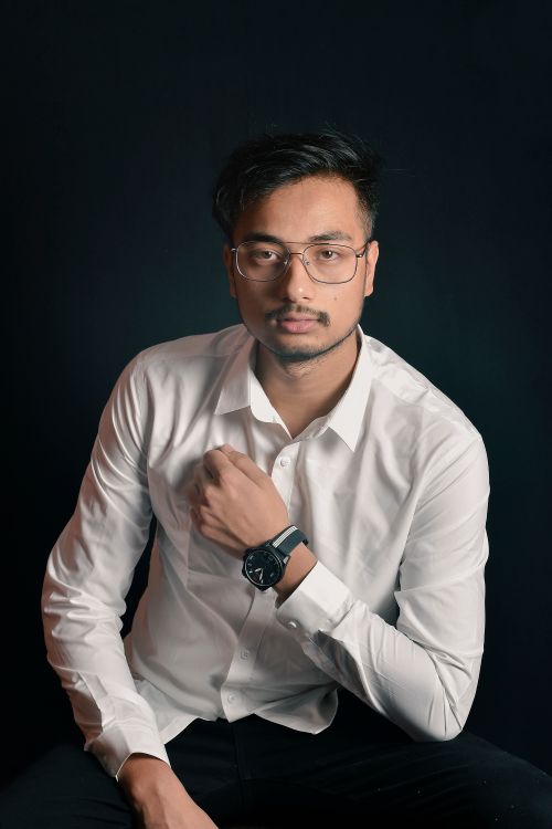 Free A young man in glasses and a white shirt posing confidently against a dark background. Stock Photo