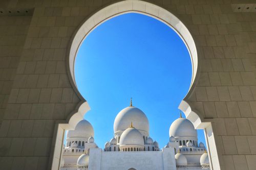 Free Elegant view of Sheikh Zayed Grand Mosque domes through a grand arch against a clear blue sky. Stock Photo