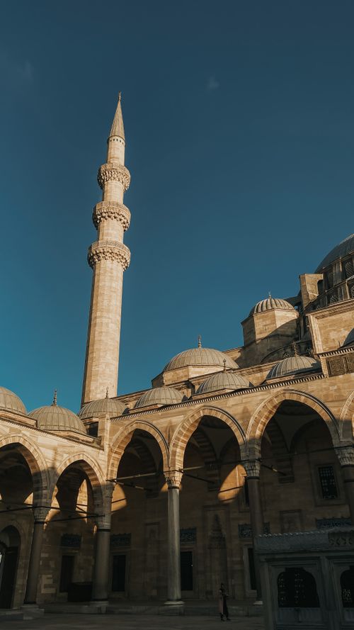 Free Elegant mosque architecture featuring a tall minaret and arches, set against a clear blue sky, perfect for travel and architecture enthusiasts. Stock Photo